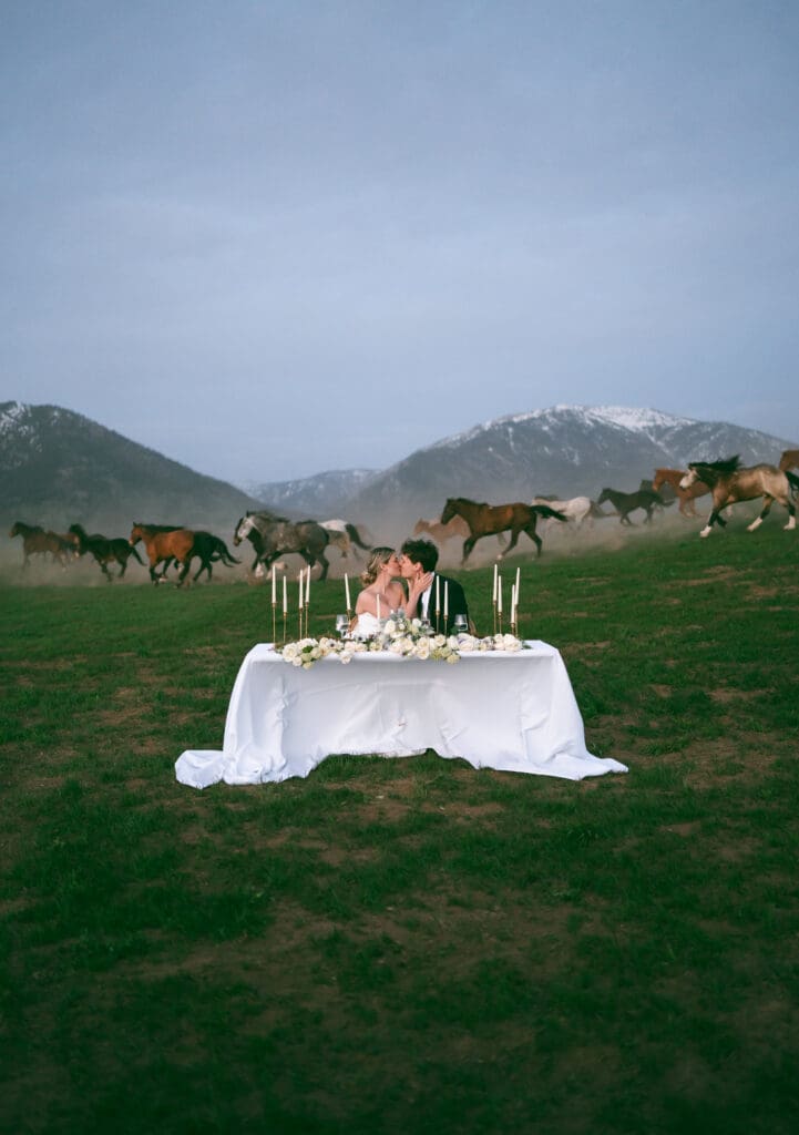 bride and groom sitting at sweetheart table with horses running behind in background